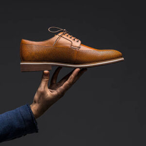 Hand holding a brown leather shoe, studio shot